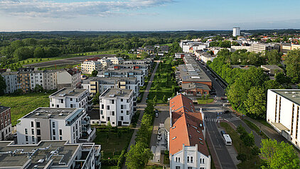 Blick auf Wohngebäude, Straßen und viel Grün unter bewölktem Himmel.