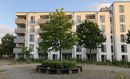 Mehrstöckiges Wohngebäude mit Balkonen und Bäumen im Vordergrund bei Tageslicht.
