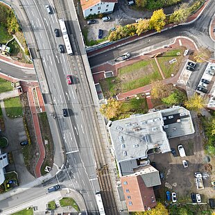 Luftaufnahme einer Brückenüberführung mit Straßenbahn, mehreren Fahrzeugen, Fußwegen und umgebenden Gebäuden