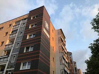 Mehrstöckiges Wohngebäude mit brauner und oranger Fassade unter bewölktem Himmel.