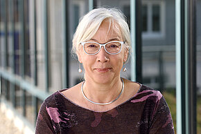 Frau mit hellen kurzen Haaren und Brille lächelt in die Kamera.