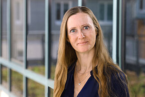 Porträt einer Frau mit langen Haaren und einem freundlichen Gesichtsausdruck, die in einem dunklen Oberteilgekleidet ist.