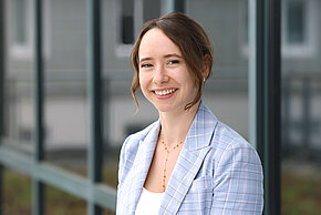 Frau mit braunen Haaren und blauen Blazer lächelt in die Kamera.