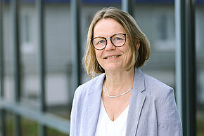 Frau mit kurzen Haaren und Brillem lächelt in die Kamera.