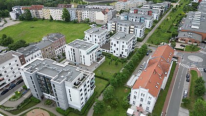 Luftaufnahme eines modernen Wohnkomplexes mit weißen Gebäuden, grünen Rasenflächen und angrenzenden Straßen.