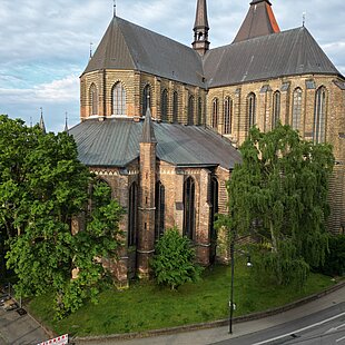 Marienkirche mit gotischer Architektur, umgeben von Bäumen und einem Gehweg unter bewölktem Himmel.
