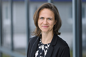 Frau mit schulterlangen braunen Haaren mit schwarzem Blazer gekleidet.