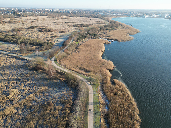 Luftaufnahme eines Wegs entlang der Warnow mit Schilf und Freiflächen